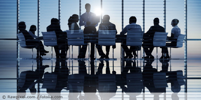 Employees having a meeting in a room full of large windows.