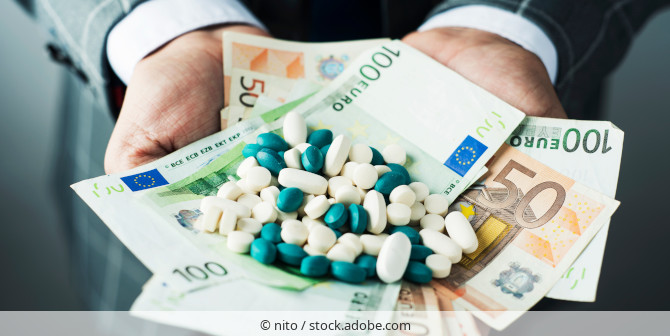 Man in a suit holding banknotes and pills in his open hands.